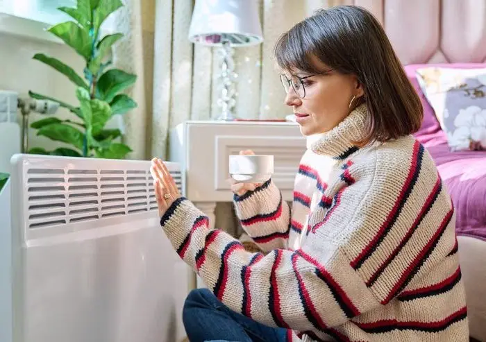 woman-warming-bedroom-near-electric-heater-middleaged-female-woolen-sweater-resting-home-near-heating-radiator-with-cup-coffee-hands-lifestyle-cold-heating-season-autumn-winter-power-repair-team